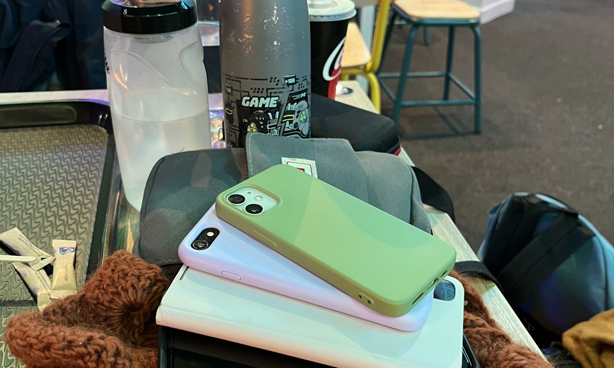 A pile of 4 mobile phones sits on a table with some water bottles.