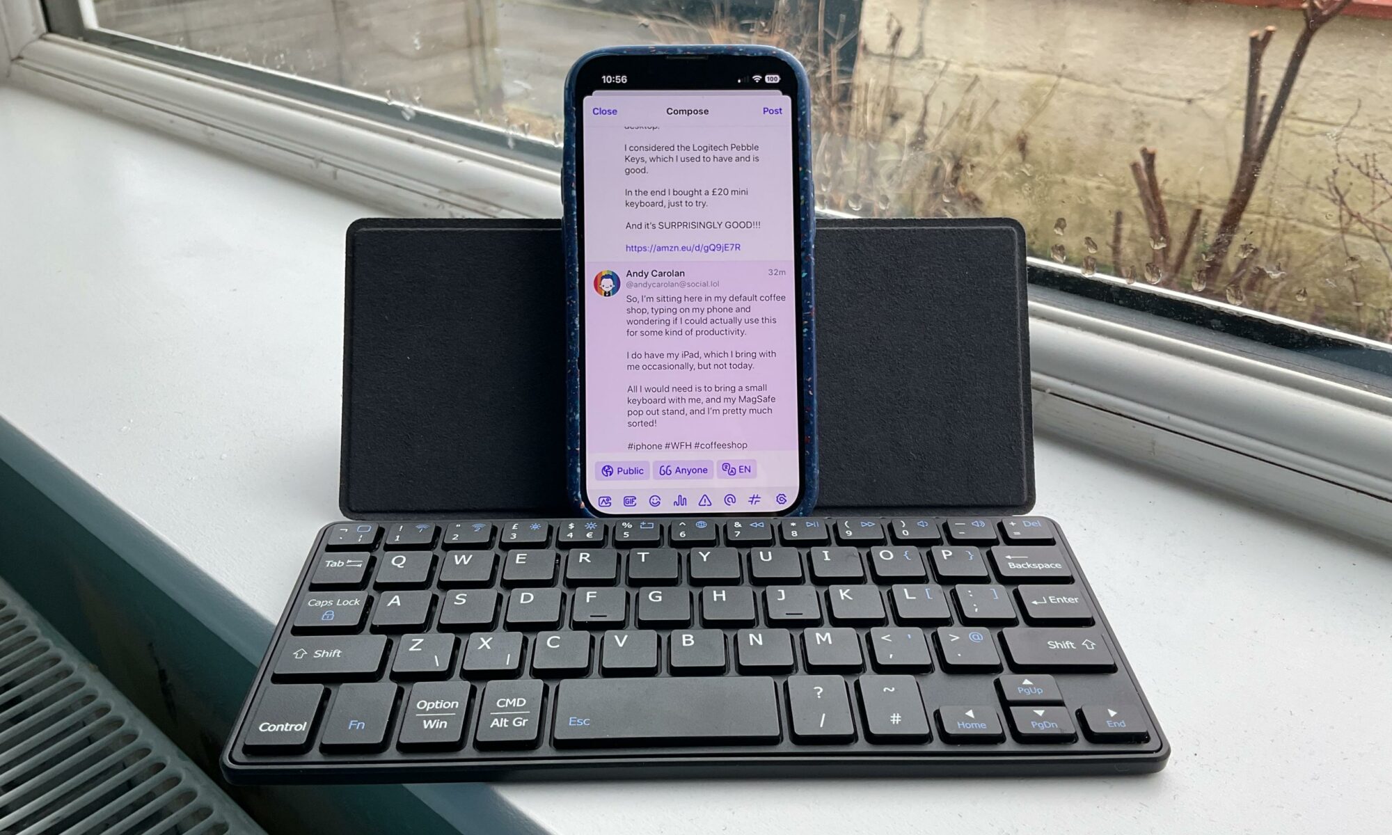 A small, pocket sized black keyboard with a built in stand. An iPhone 13 mini rests on the stand.