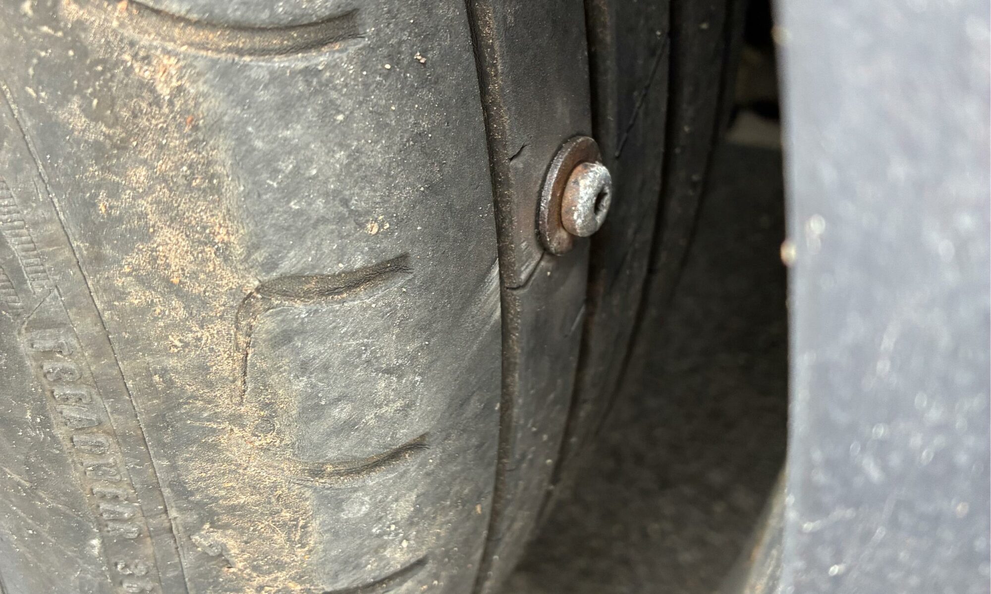 A close up of a car tyre with a big screw stuck in it.